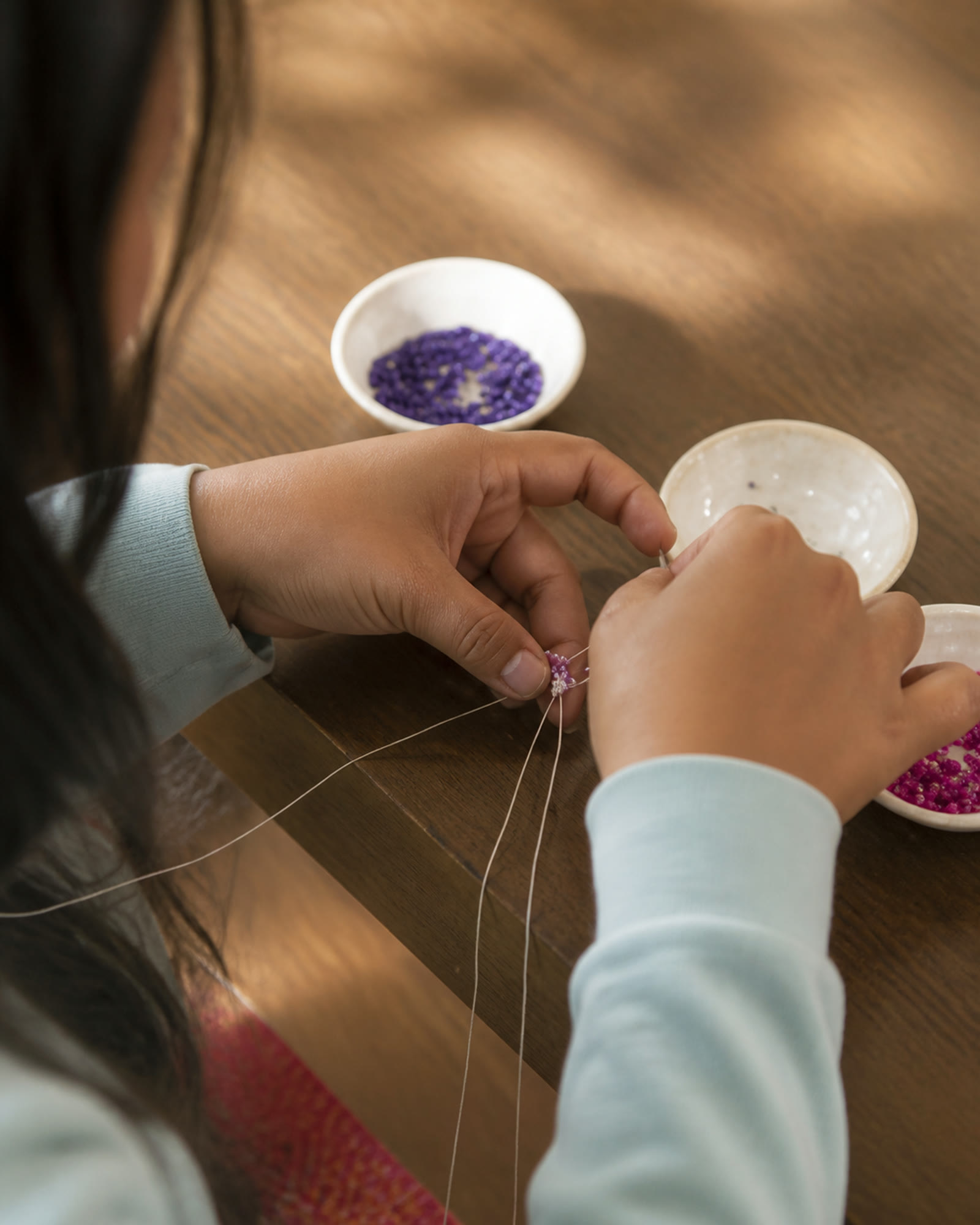 A bead artisan threading purple and pink glass seed beads by hand