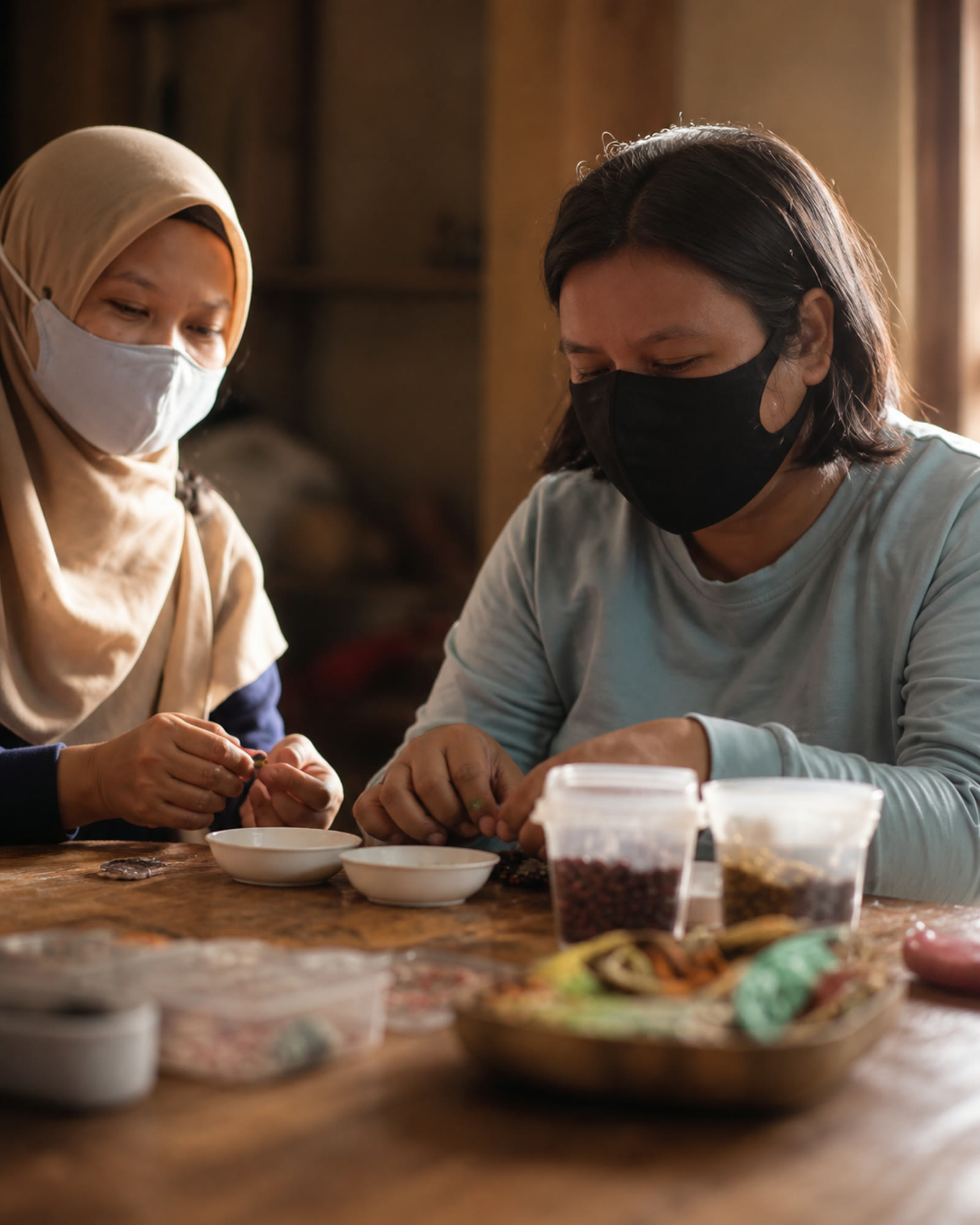 Two women sorting and threading beads together at a wooden worktable